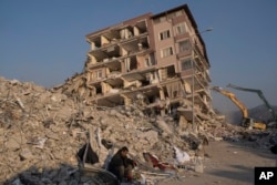 Un hombre se sienta en los escombros de un edificio derrumbado por los sismos recientes, el domingo 12 de febrero de 2023, en Antioquía, Turquía. (AP Foto/Petros Giannakouris)