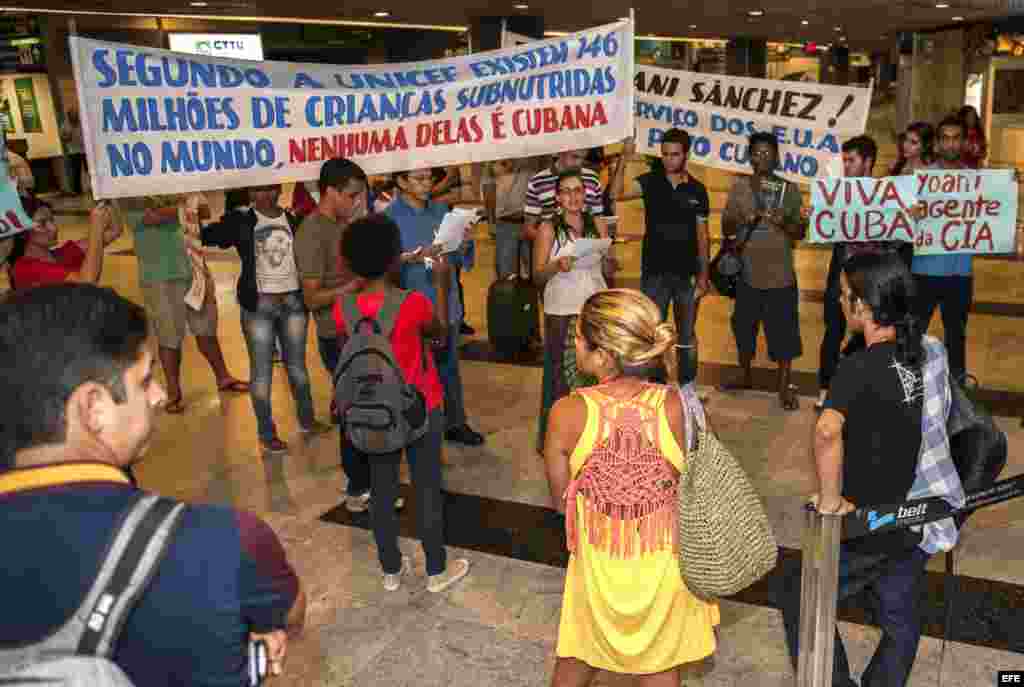 La disidente cubana Yoani Sánchez (d), autora del blog "Generación Y", recibe del cineasta Dado Galvao (i), su anfitrión en Brasil, una cinta de "Senhor do Bonfim" hoy, lunes 18 de febrero de 2013, en el aeropuerto internacional Guararapes, de la ciudad d